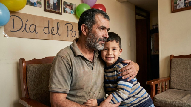 fotografía cercana de una celebración familiar del Día del Padre en Colombia, padre abrazando a su hijo en un salón sencillo con decoración modesta que incluya la frase