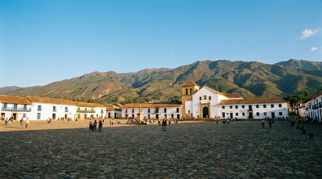 Una vista panorámica de la Plaza Mayor de Villa de Leyva en Boyacá, mostrando su suelo empedrado, la iglesia colonial blanca al fondo y las montañas andinas bajo un cielo despejado