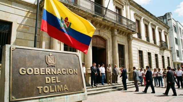 Placa institucional de la Gobernación del Tolima frente al edificio del palacio departamental, con una bandera del Tolima ondeando y personas entrando al lugar durante un acto prot
